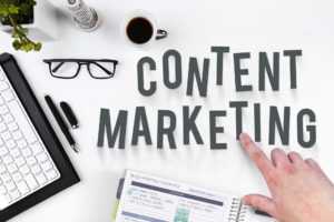 the words content marketing near a laptop, glasses, and folders